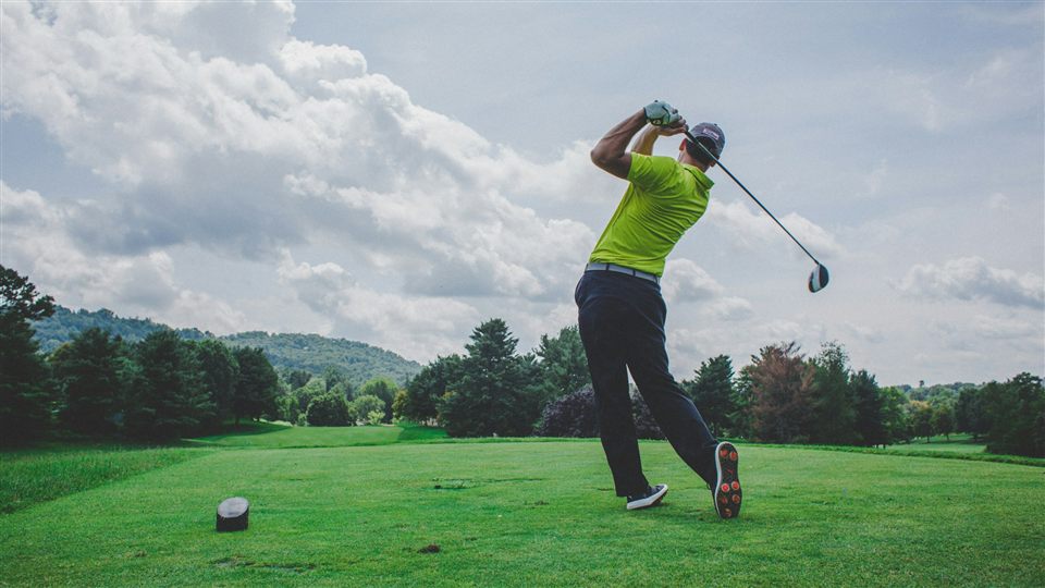 A golfer mid-swing on an overcast day with hills in the background