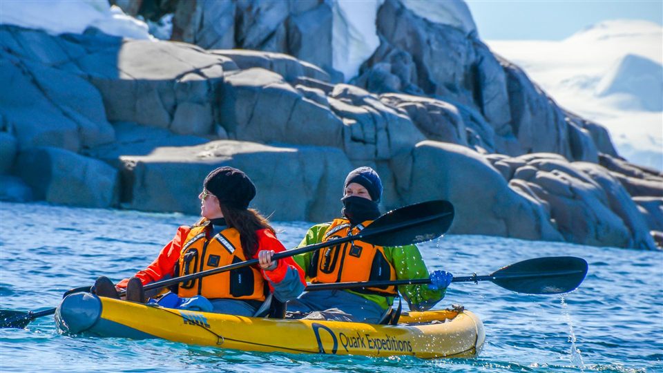 Two people kayaking through icy glacier waters